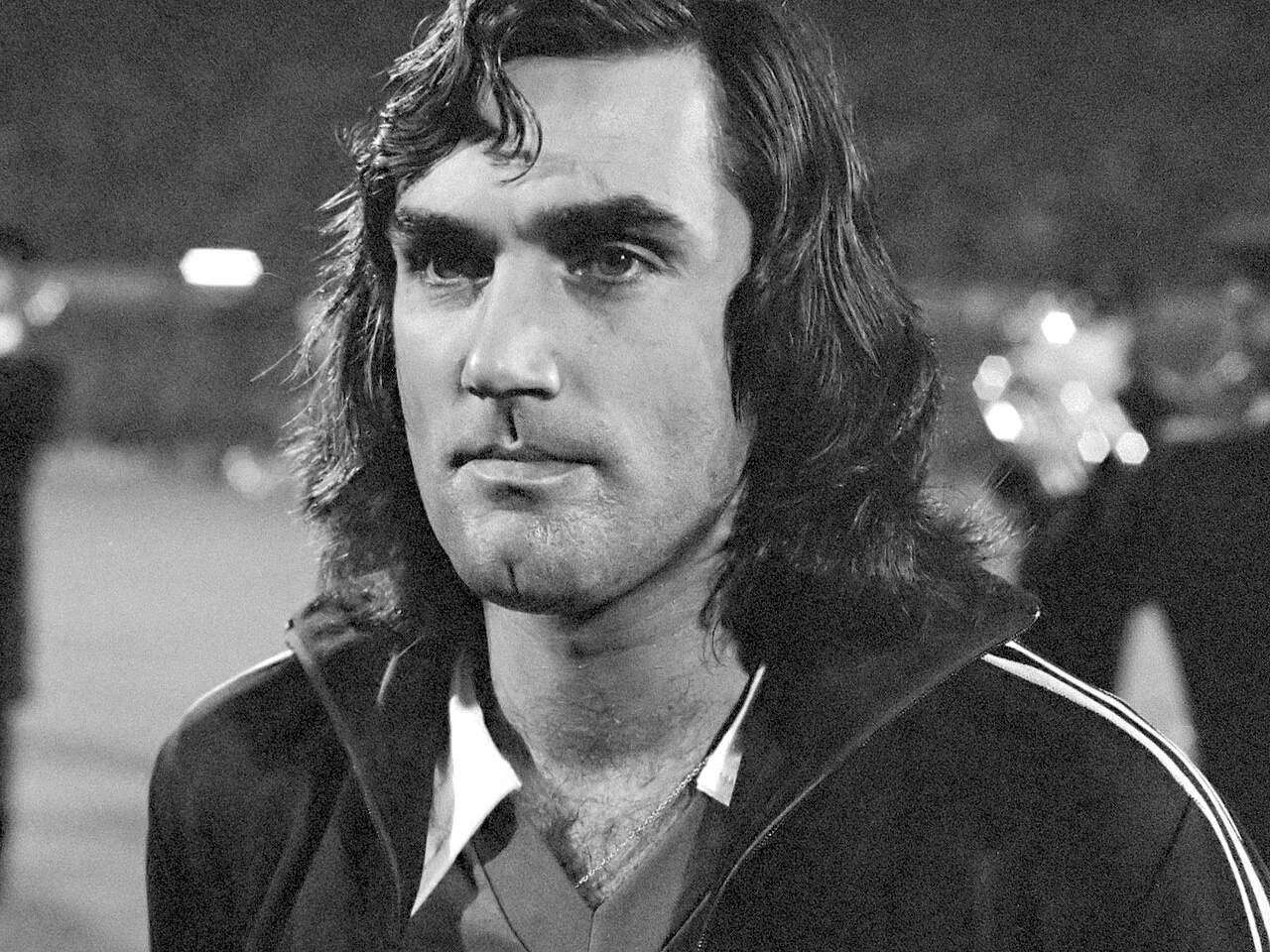 George Best i träningsjacka på en upplyst fotbollsarena, svartvitt foto från 1976